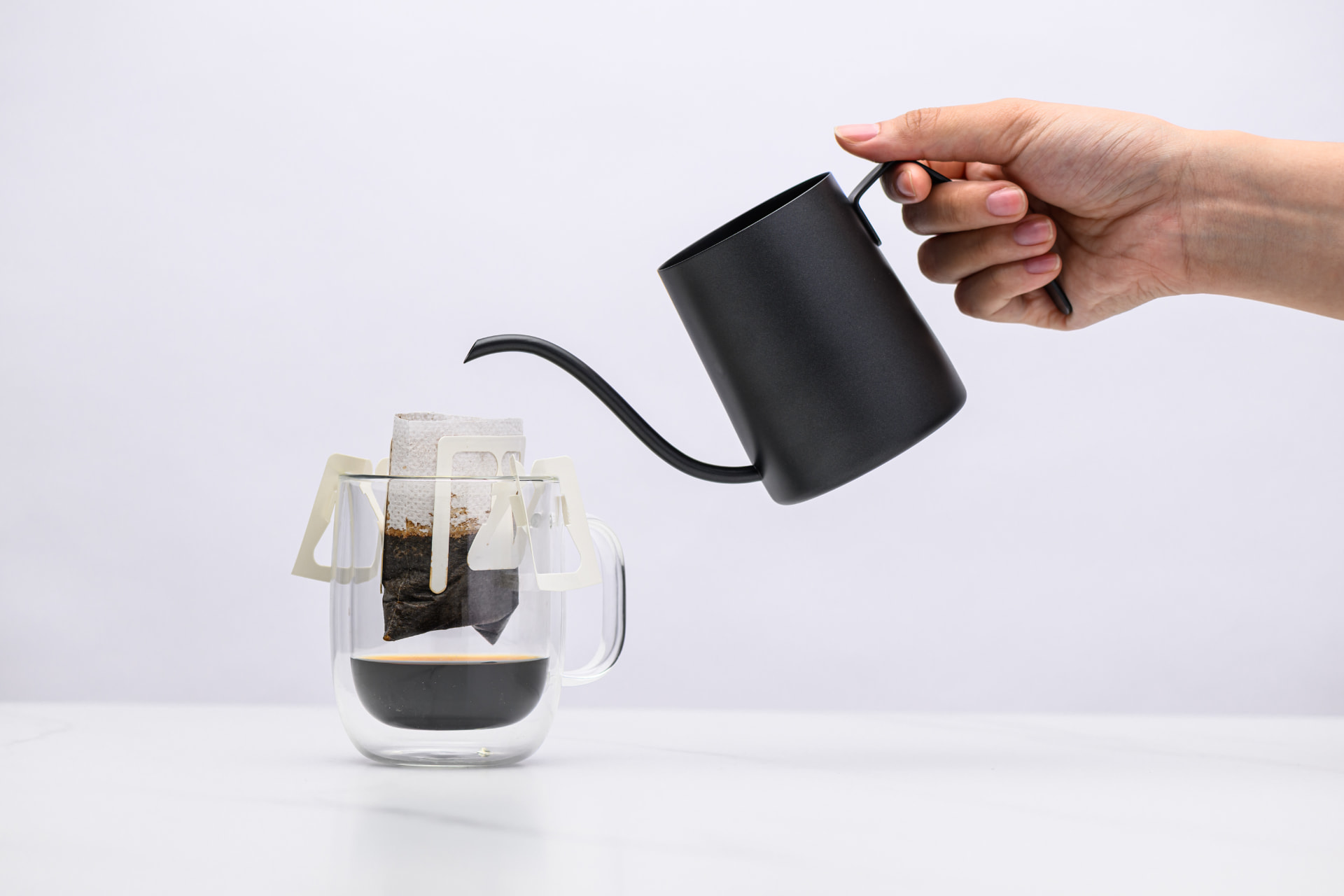 Hot water being poured from a black gooseneck kettle into a Sampan drip bag resting on a g